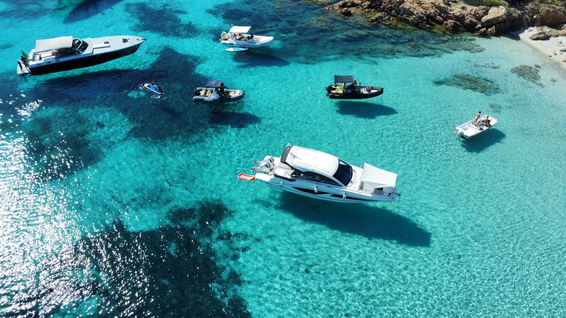 Motor yachts anchored in clear turquoise water beside a Sardinian cove